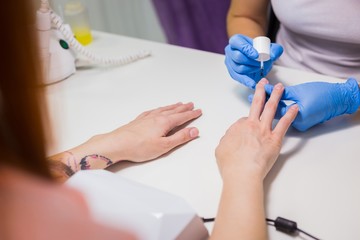 Professional beautician applying nail polish to female nail in a nail salon.