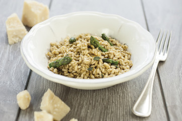 Asparagus Risotto in ceramic plate on wooden table with silver fork and pieces of Parmesan cheese