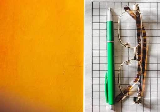 Pen, Glasses And Crossword Puzzle On A Yellow Table - Top View