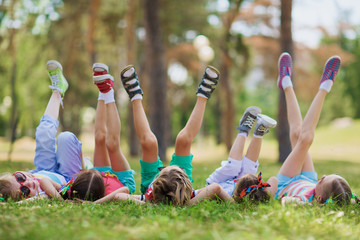 Children lying on green grass in park on a summer day with their legs lifted up to the sky