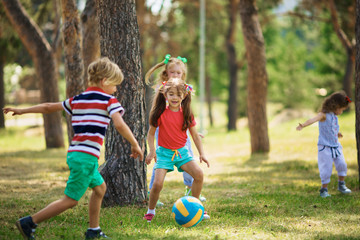 Little kids playing soccer on green lawn in park on a wonderful summer day