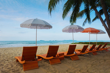 Orange beach chairs and parasols on sandy beach with cloudy blue sky and sea