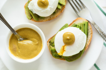 Vegetarian breakfast: avocado toast with poached eggs and mustard, orange juice,muffin on white wooden background. Selective focus
