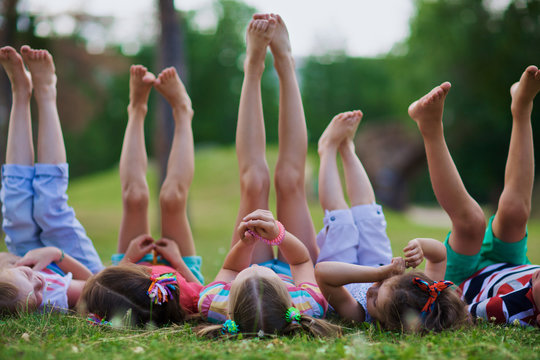Kids lying on green grass barefoot and enjoying summer day with legs lifted up to the sky