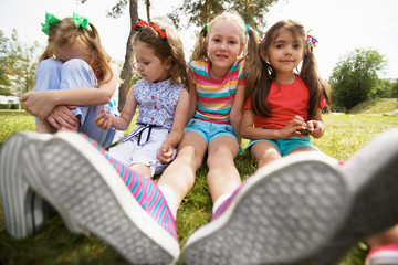 Low angle view of pretty little girls in sneakers resting on green lawn in park on a warm summer day