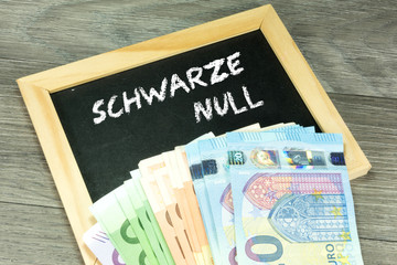 Euro Geldscheine und eine Kreidetafel mit dem Text Schwarze Null