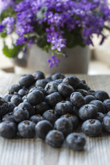 Fresh blueberries are on the wooden background with violet flowers as background