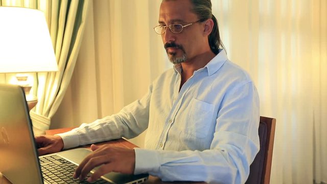 middle age attractive handsome man with glasses using laptop and taking notes at home office
