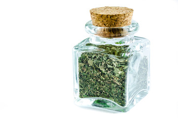 Dry parsley herb in glass bottle isolated on white background. Closeup macro shot. 