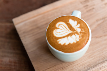 heart and wing latte art pattern in white cup on wooden table