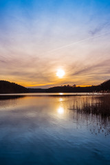 Fototapeta premium Setting sun over a tranquil lake with reeds