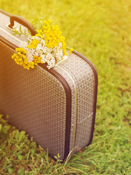 Old gray suitcase and bouquet of yellow wild flowers on a green grass in summer sunny day. Conceptual image of tourism, travel