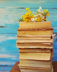 Pile of old books with a bouquet of yellow flowers tansy and yarrow on a blue background
