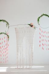 Interior design with weaving and flowers. Spring dream catchers with green leaves and red brushes. Wicker arch on a branch