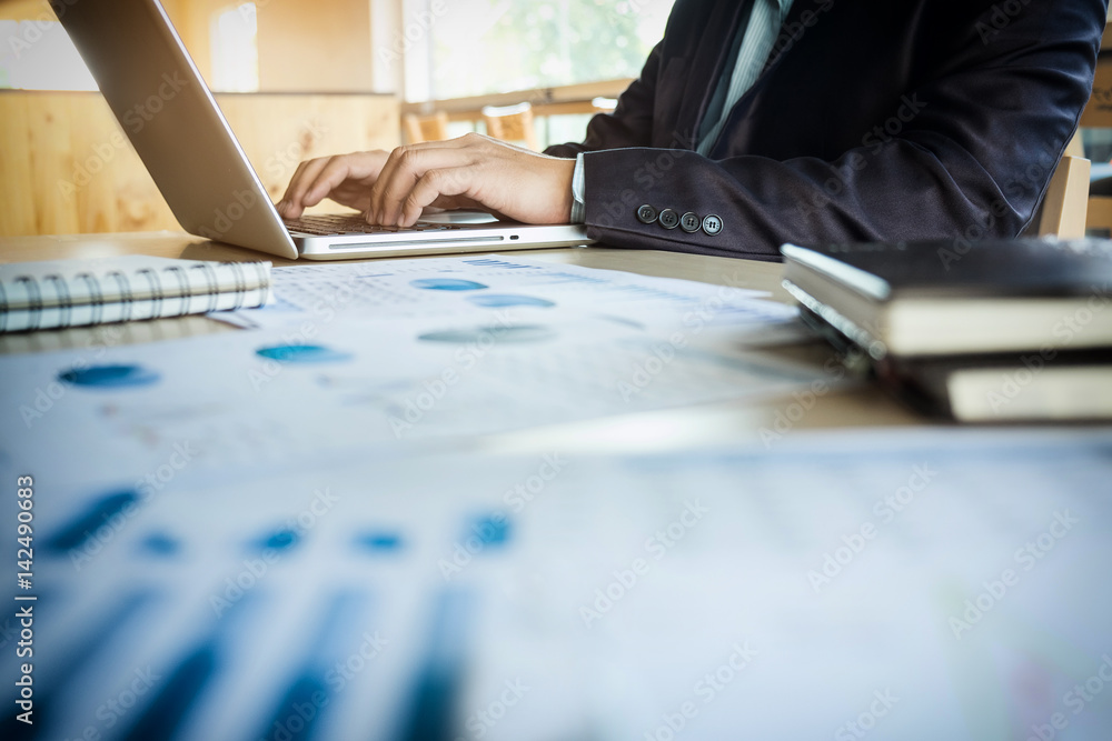 Wall mural young business manager working at office with laptop and financial data documents on his desk.