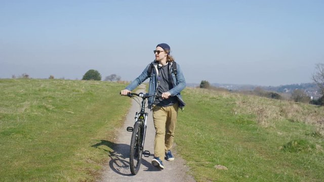 4K Wide angle shot of hipster walking with his bike in the country, in slow motion