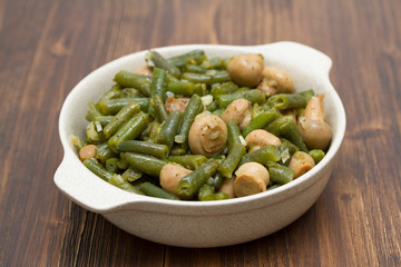 green beans with mushrooms in dish on wooden background