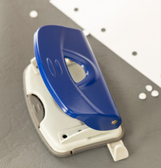 Close up capture of navy blue hole puncher, white paper on grey ground at office
