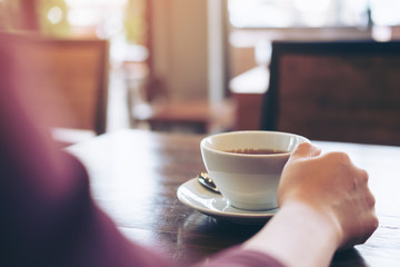 Woman holding a cup of coffee on wooden table in modern loft cafe
