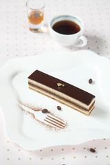 Piece of "Opera" Chocolate Coffee Cake on square white plate and cup of coffee, on light background.