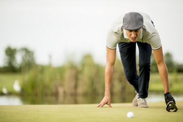 Young man looking at ball while crouching on golf course