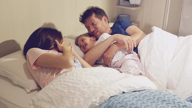 Family in bed tickeling with little daughter retro style