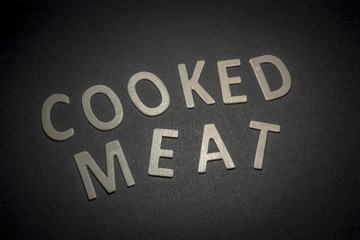 Cooked meat written with wooden letters on a black background