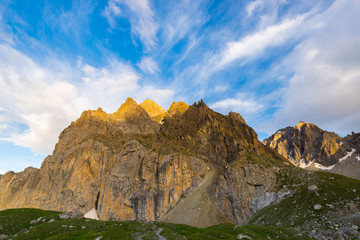 Last warm sunlight on alpine valley with glowing mountain peaks and scenic clouds. Italian French Alps, summer travel destination.