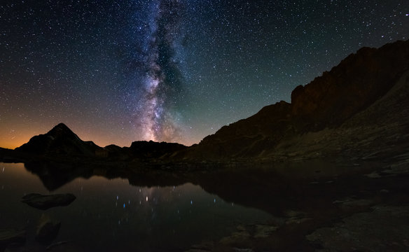 The outstanding beauty of the Milky Way arc and the starry sky reflected on lake at high altitude on the Alps. Fisheye scenic distortion and 180 degree view.