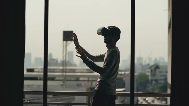 Silhouette of young man watching movie in VR headset and have virtual reality experience on hotel room balcony