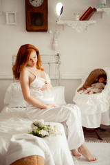 Fototapeta na wymiar Pregnant woman with red hair in white dress in children's room