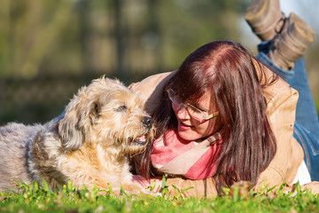 young woman lies with her dog in the grass