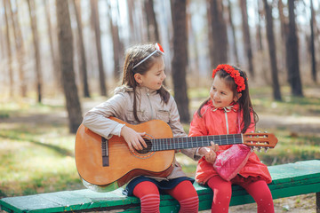 Two little sisters singing and playing the guitar sitting on the bench