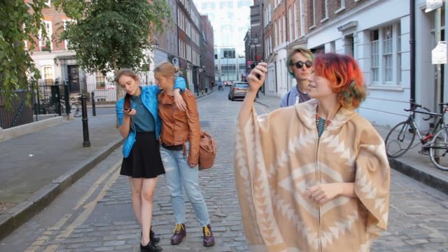 Four friends are walking the streets of London. Do selfies, laugh and fool around. On summer vacation.
