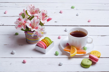 Spring composition: a cup of tea, almond cookies, bright flowers on a wooden table.
