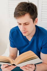 Man reading a book sitting on the bed