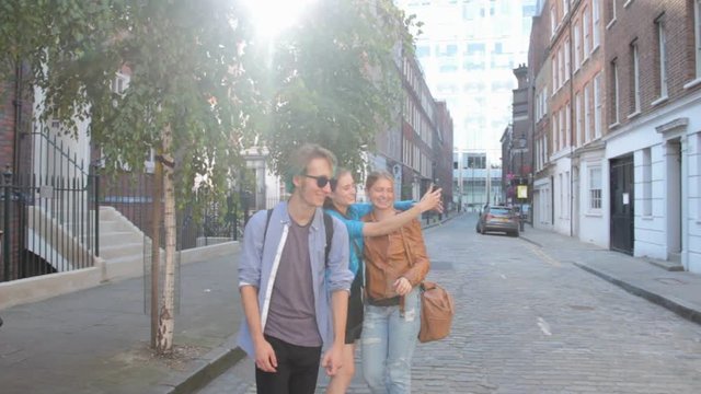 Four friends are walking the streets of London. Do selfies, laughing and joking. On summer vacation.