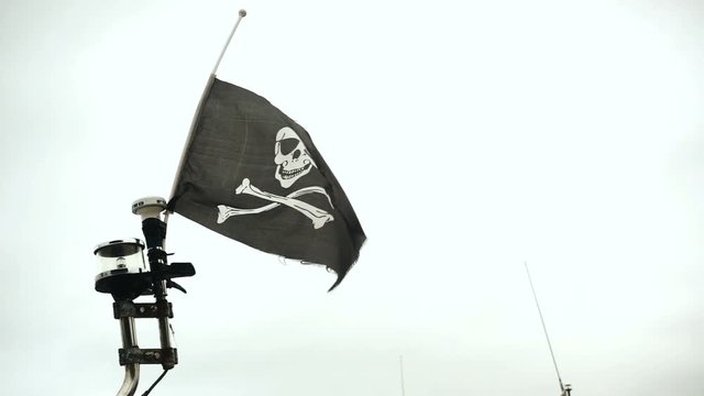 Waving black flag with skull and crossbones symbols over cloudy sky, Jolly Roger pirate flag waving slow motion 240 FPS
