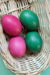 four colored easter eggs in basket on green background