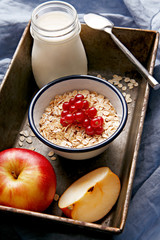 Cereals decorated with currants on a wooden platter. Bottle of fresh milk and apples. Healthy breakfast.