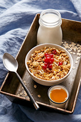 Cereals bowl decorated with currants on a wooden platter. Bottle of fresh milk in the background, honey in the foreground. Healthy breakfast.