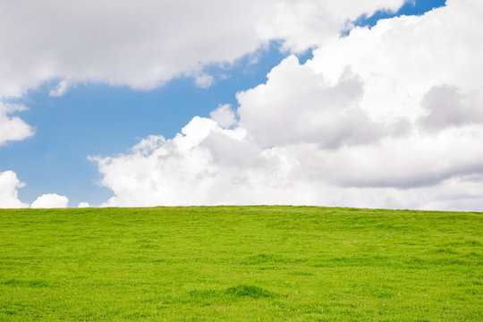 Grassy Hill With White Clouds And A Blue Sky