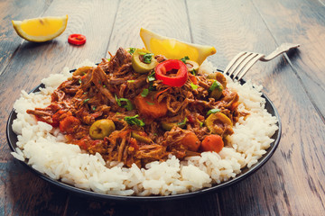 Slow Cooker Ropa Vieja, Cuban famously delicious shredded beef stew with pepper and olives on a black plate with a boiled rice and fresh lemon on the wooden table. - 142505409