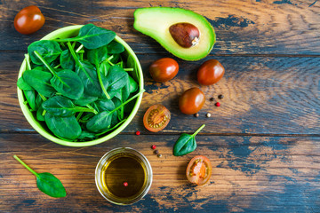 Organic ingredients and olive oil for vegetable vegetarian salad with fresh avocado, tomatoes and spinach on the wooden rustic background, top view.