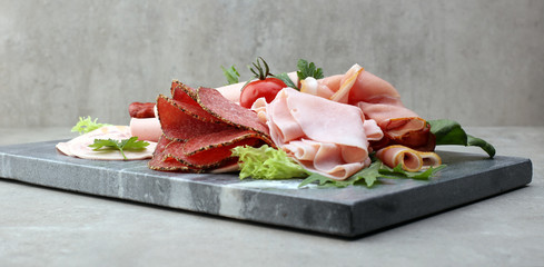 Food tray with delicious salami, pieces of sliced ham, sausage, tomatoes, salad and vegetable - Meat platter with selection