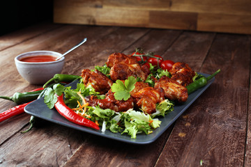 barbecue chicken wings close up on wooden tray with red spice sauce and salad