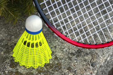 Neon green shuttlecock and red badminton racket leaning on stone wall, closeup