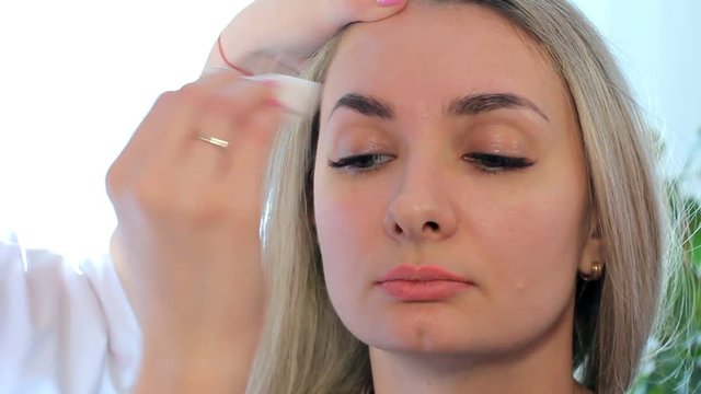 Cosmetologist washes away paint from eyebrows a cotton disk. End of the procedure.