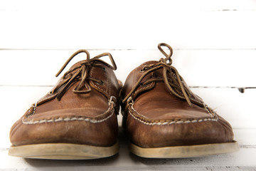 Pair of worn out brown casual leather shoes in front of white wooden background