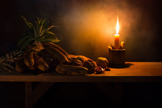 Withered and rot fruits on wooden plate with dim light candle in the night